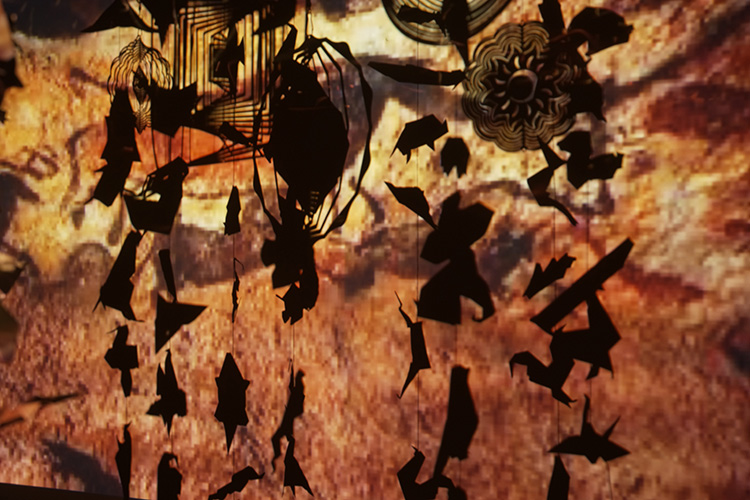 鉄と和紙で作られた動物のモビール作品、背景に洞窟壁画の映像が投影されたインスタレーション