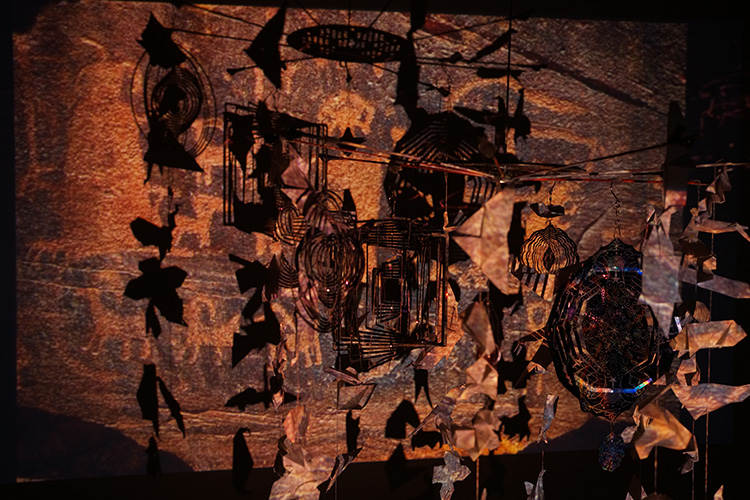 鉄と和紙で作られた動物のモビール作品、背景に洞窟壁画の映像が投影されたインスタレーション